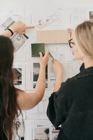 Two people working on a design project with design presentations, concept boards, material samples and notes on a whiteboard.